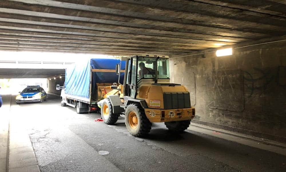 Ein Bagger probiert einen unter einer Bahnunterführung festgefahrenen LKW zu befreien